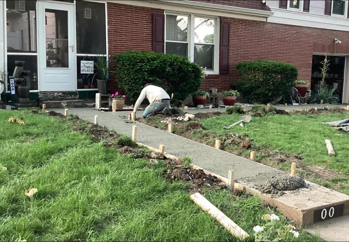 Man smoothing wet concrete walkway in front of a house.