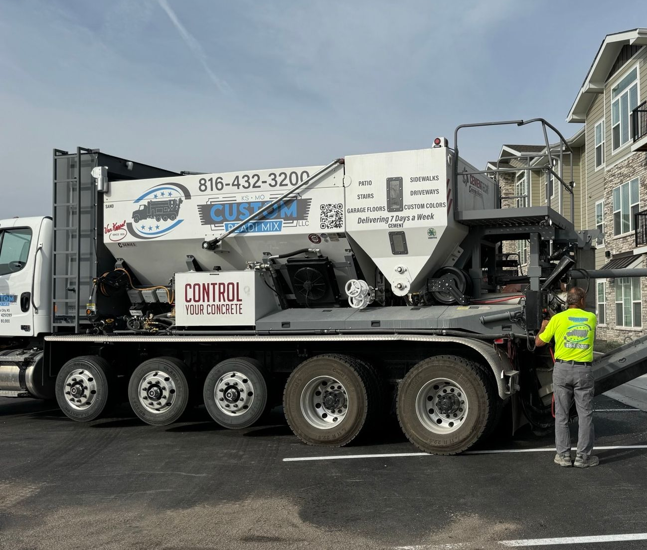 Large industrial truck with concrete mixer equipment parked on a street, worker in neon vest standing beside it