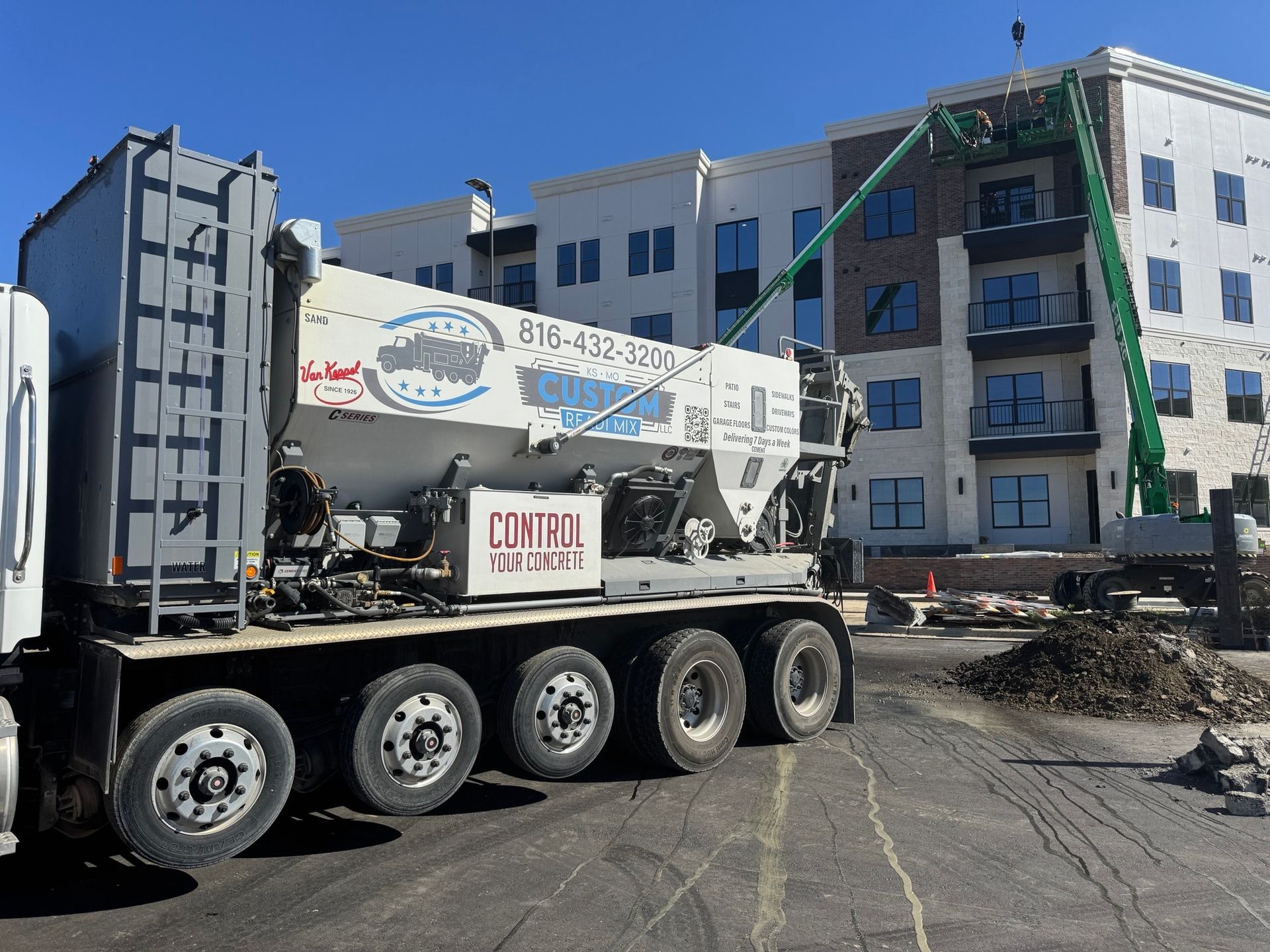 A concrete pump truck parked at a construction site in front of a multi-story apartment building under a clear blue sky.