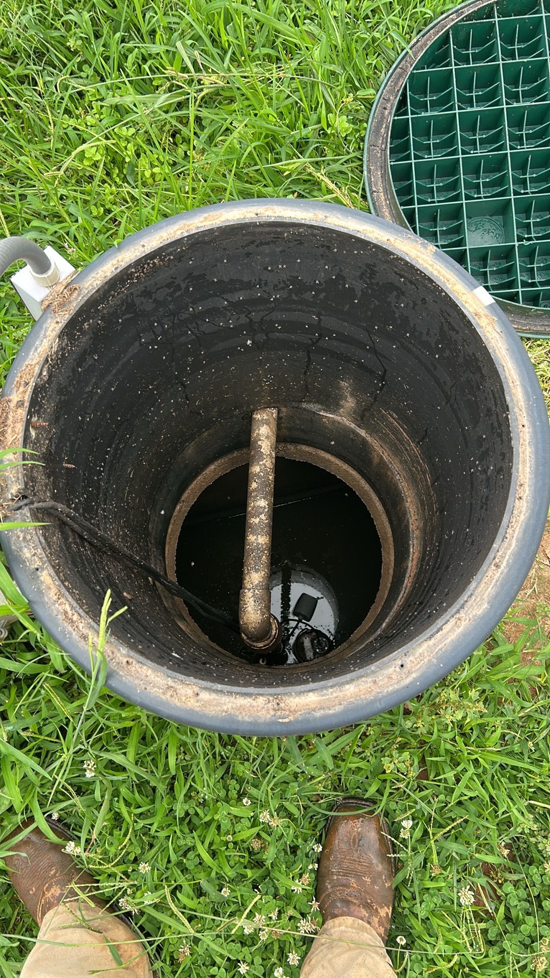Open septic tank, showing a dark interior and water, with a pipe and pump visible. Someone is standing nearby.