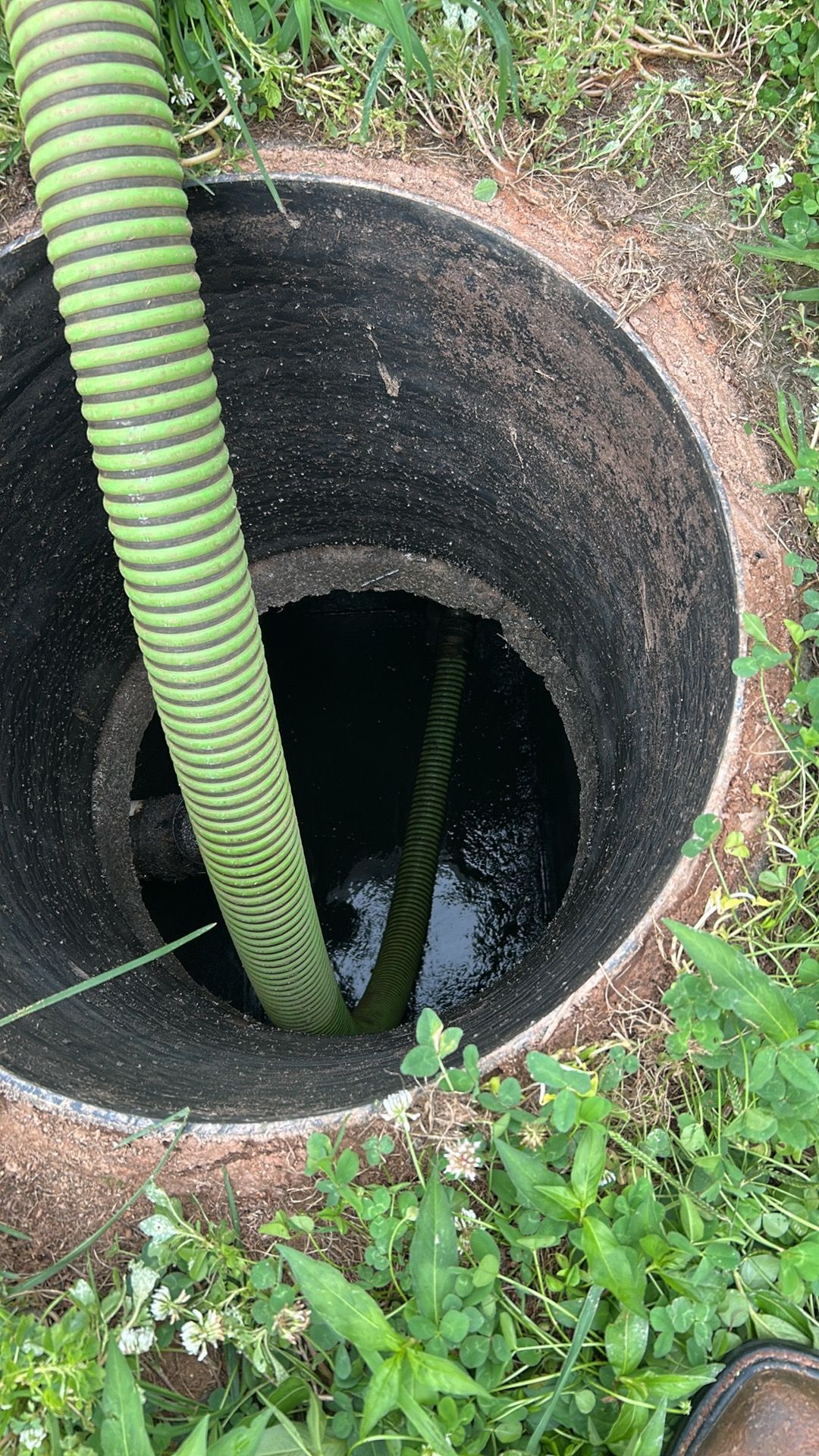 A concrete septic tank is open, with a green hose inside. It's surrounded by grass.