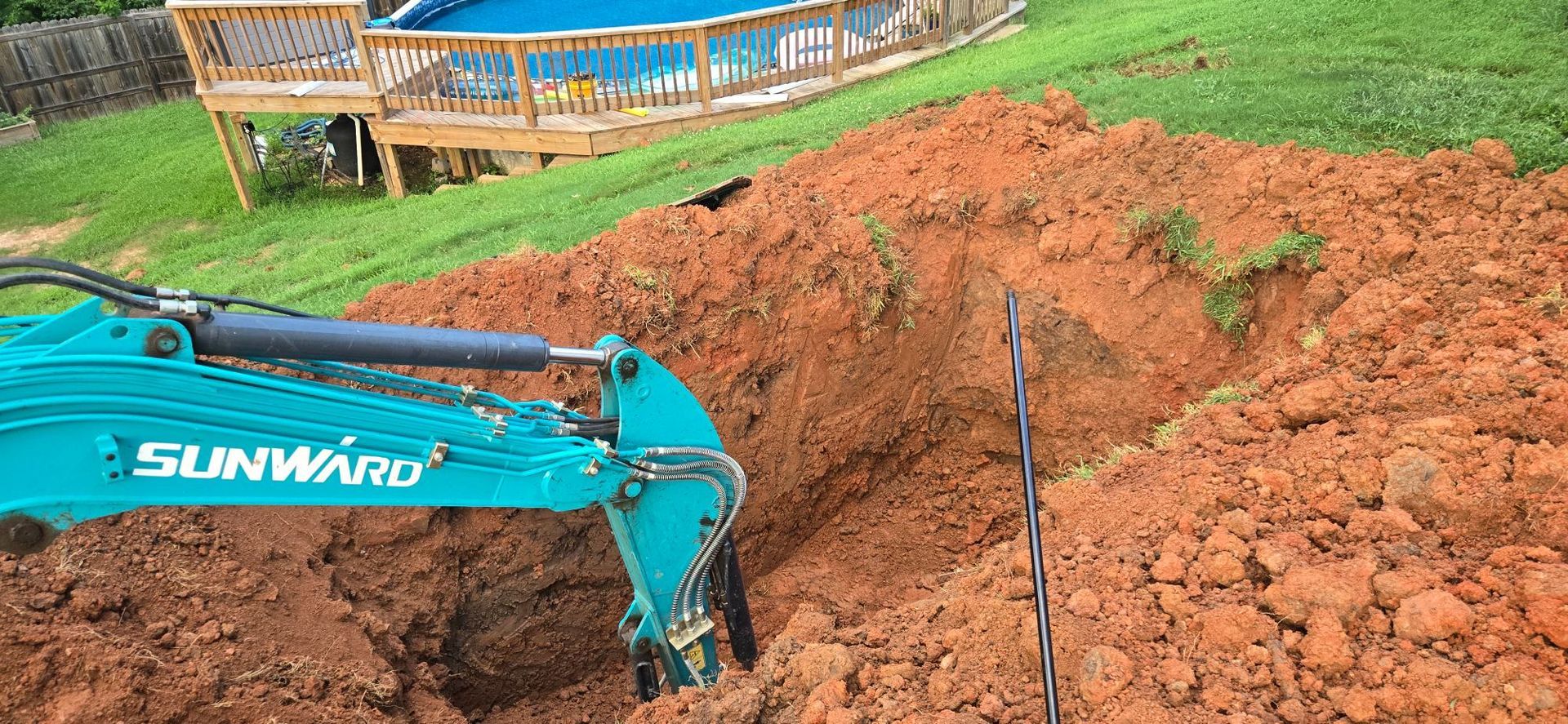 Turquoise excavator digging a large red dirt mound at a construction site