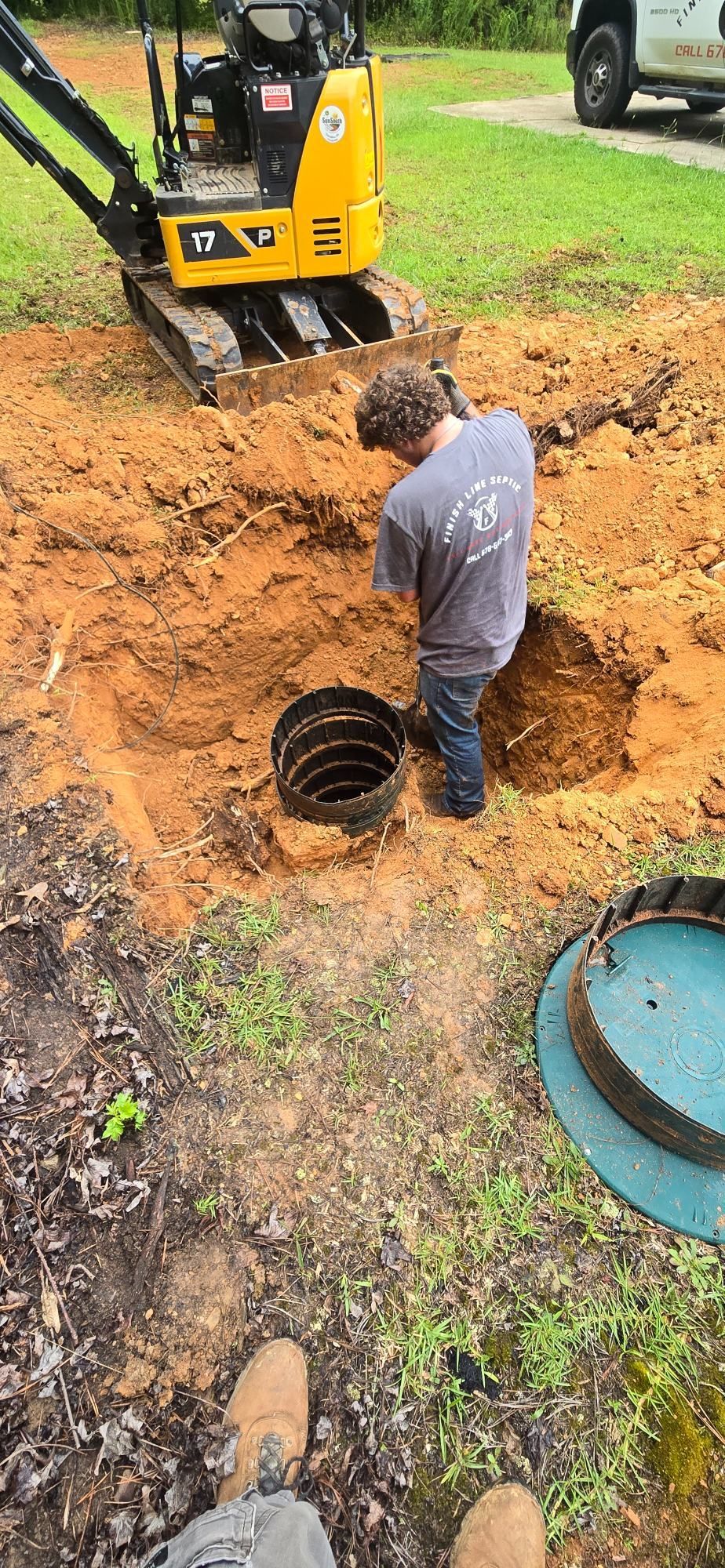 Worker inspecting a black pipe in a muddy trench beside a yellow excavator