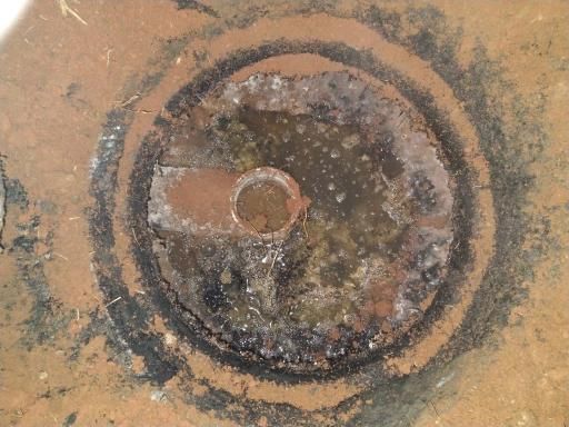 Rusty circular metal drain cover with a small hole in the center on a textured tan surface