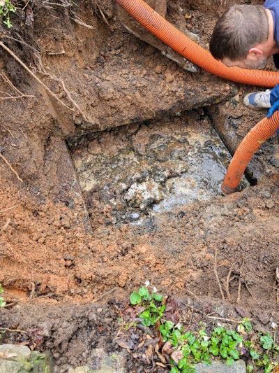 Man examining an exposed rock formation in a dirt excavation. Orange hose is visible.