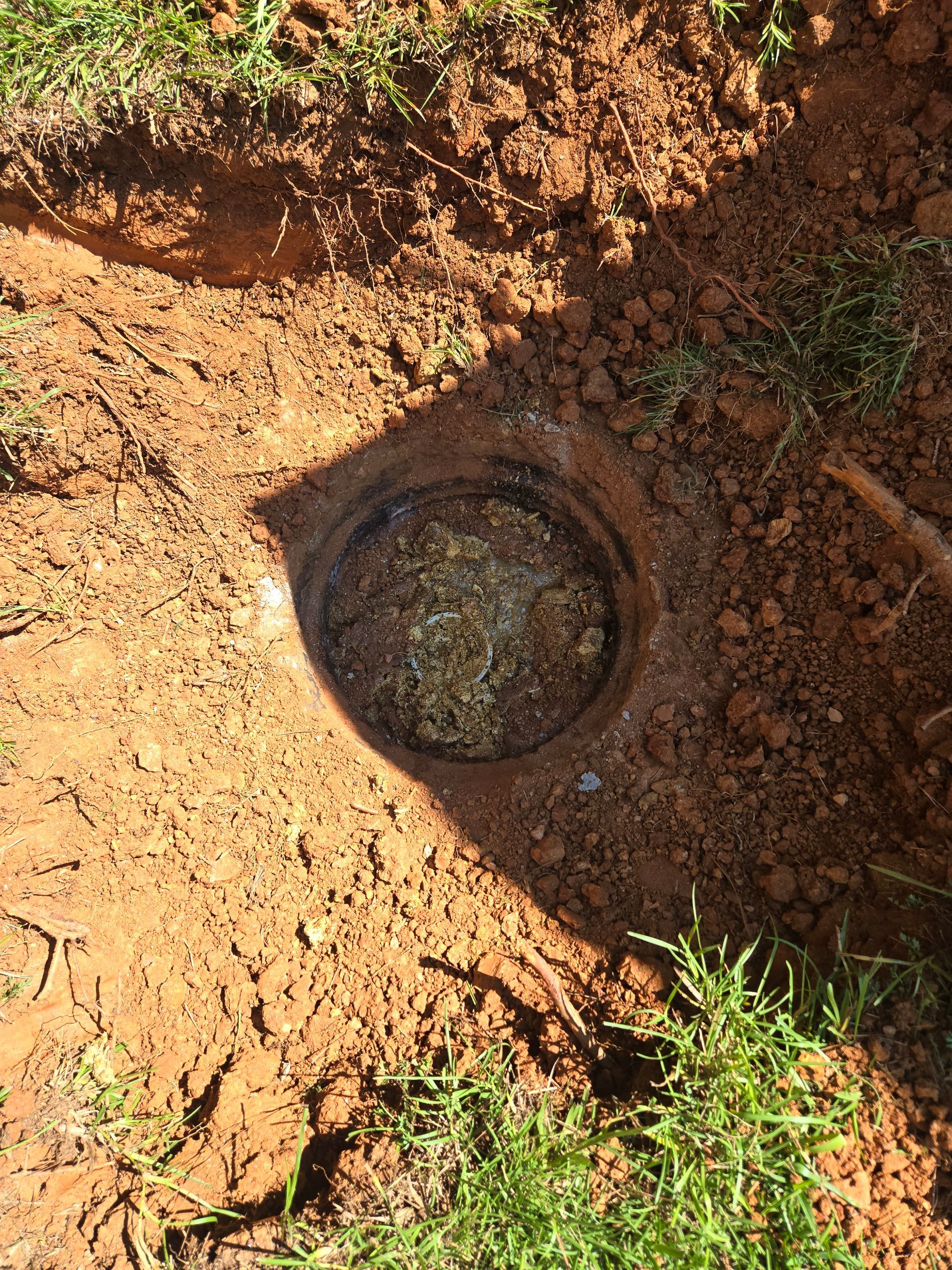 A circular opening in the ground surrounded by dirt and grass, possibly a well or access point.