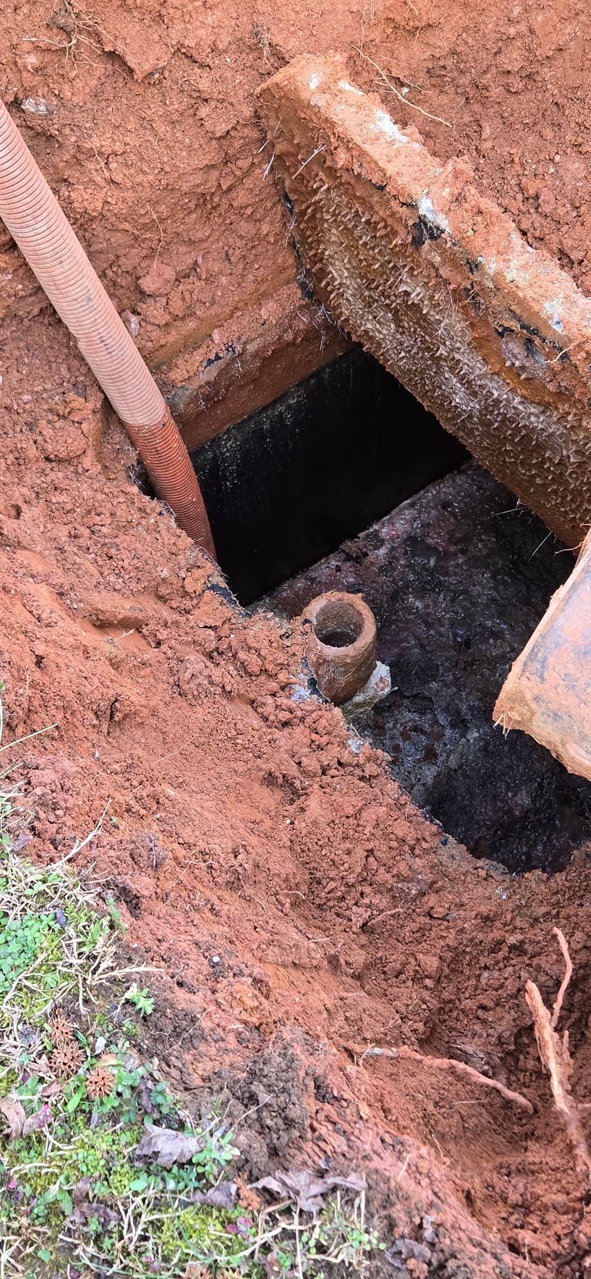 A hole in the ground with a pipe is revealed; the hole's sides are red dirt. A rusty lid sits above the dark space.