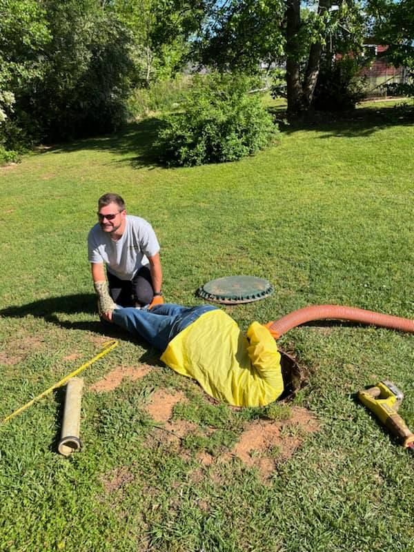 Two men working on a septic tank in a grassy yard.