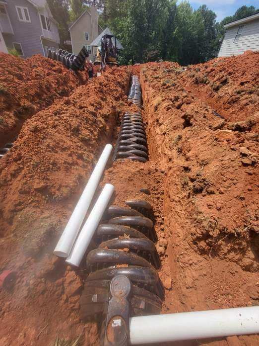 Construction site: a trench dug in red dirt holds connected black plastic rings.