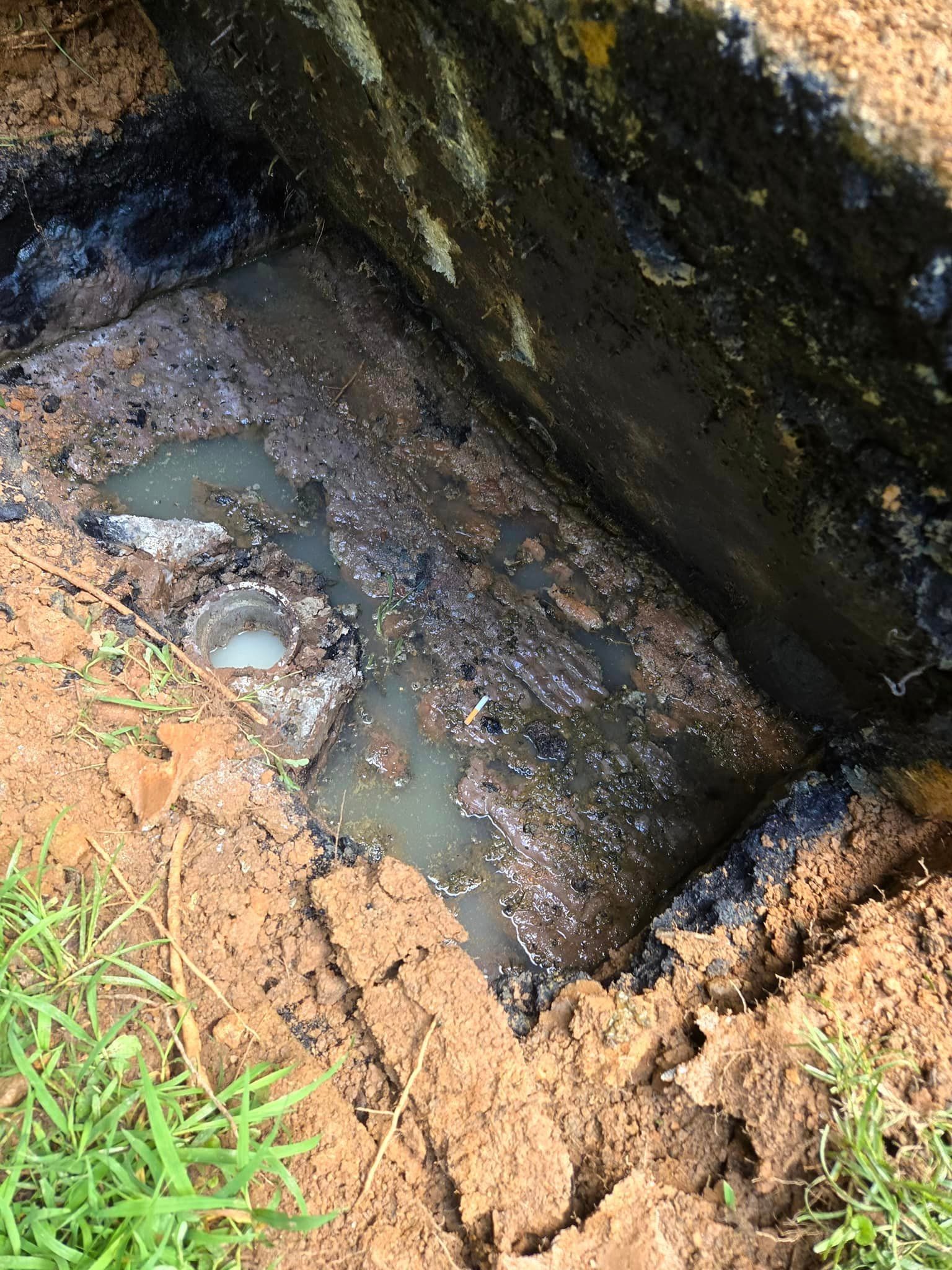 Open rectangular septic tank partially filled with murky water and sludge. Brown dirt surrounds the concrete structure.