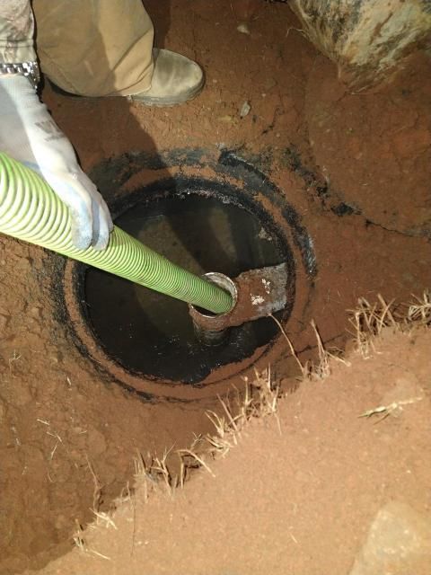 Worker inserting green hose into a buried black pipe opening in a dirt trench