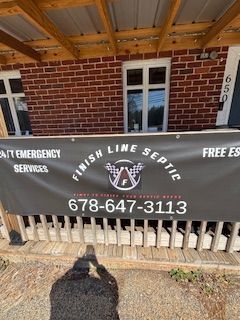 Black banner for Finish Line Septic with phone number. It's hanging in front of a brick building with a porch.