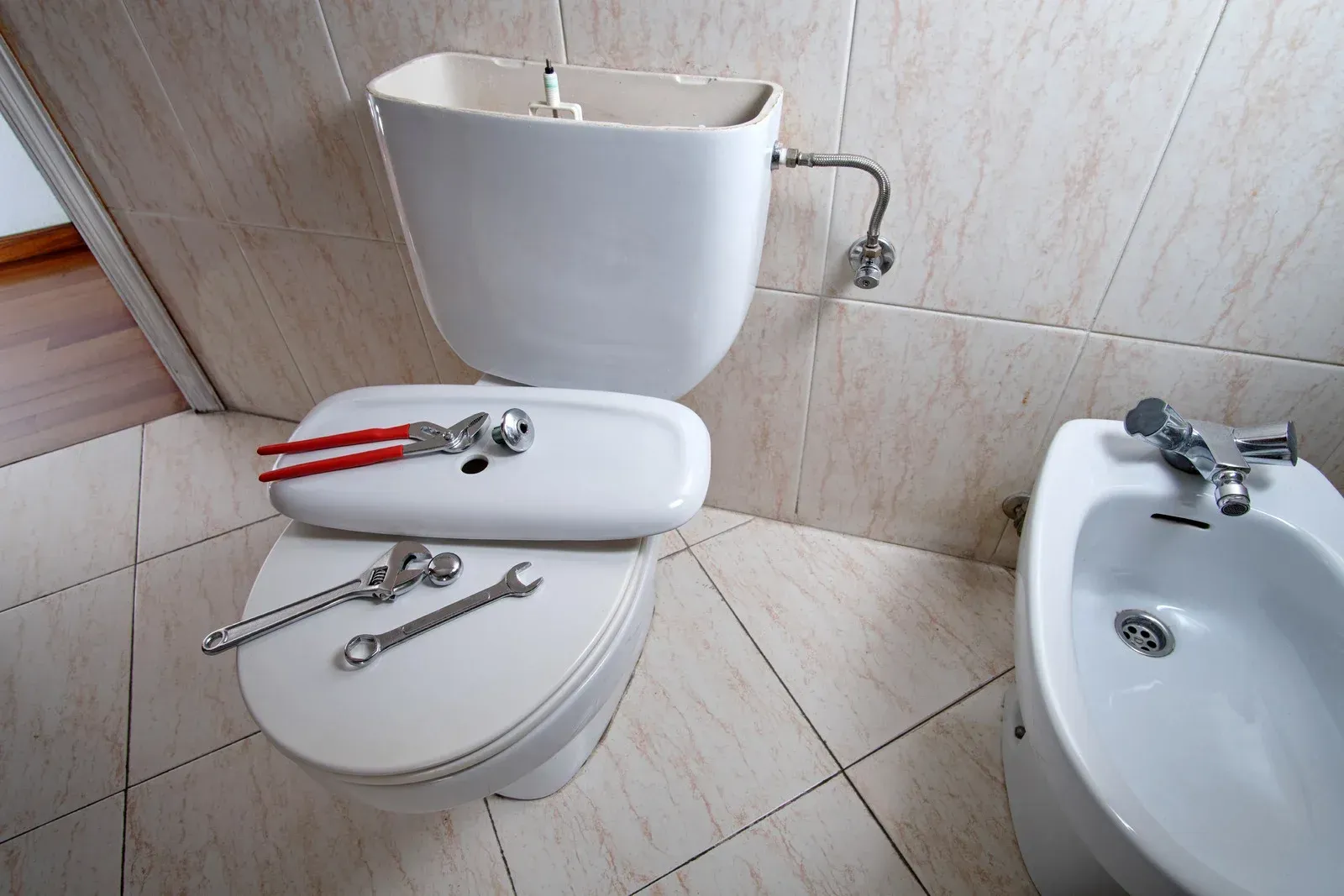 Toilet with lid removed, tools on it, and the tank exposed, in a bathroom.
