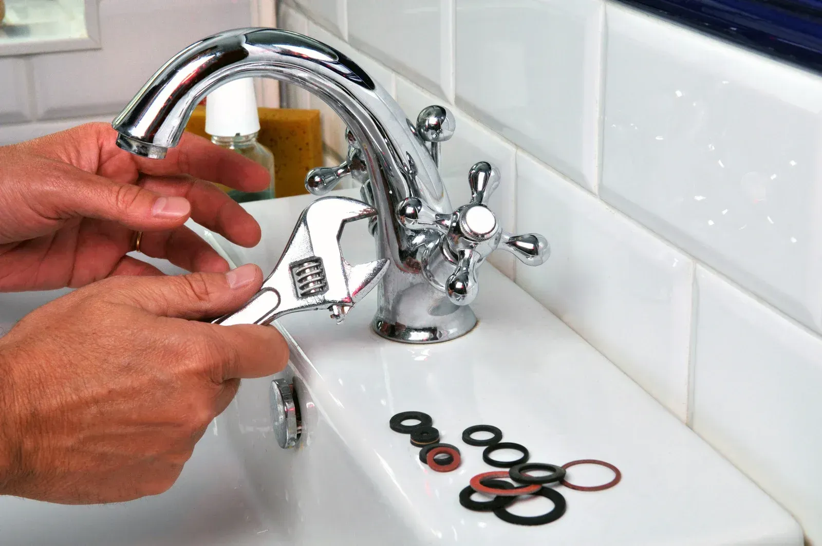 Person using wrench to repair a chrome faucet in a white sink. O-rings are in front.
