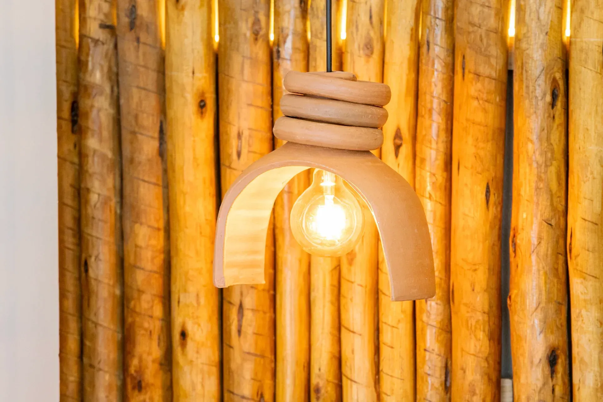 Lâmpada pendente com luz quente em um abajur de madeira contra uma parede de bambu.