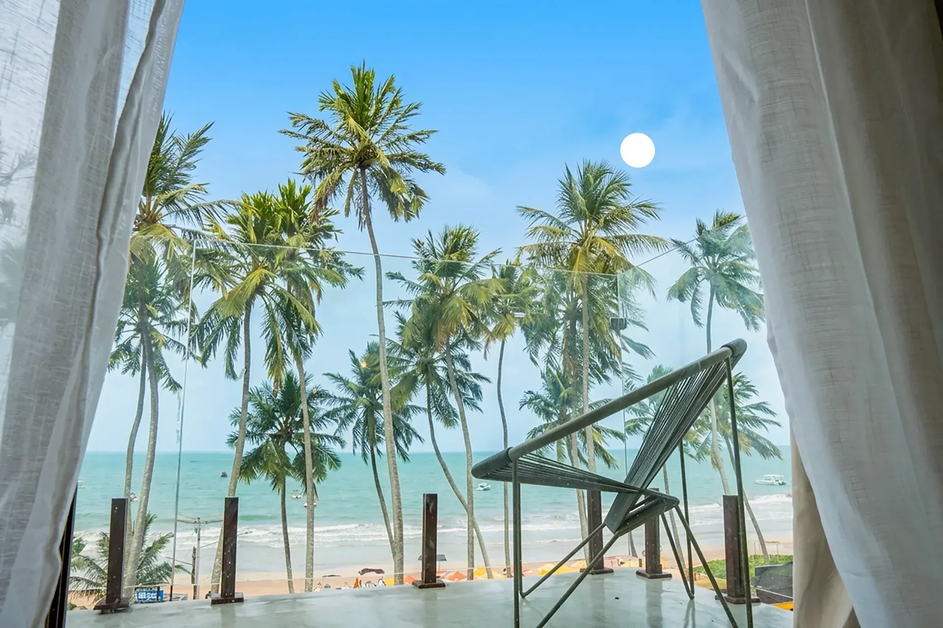 Vista de uma praia tropical com palmeiras, água turquesa e um toldo branco na orla.