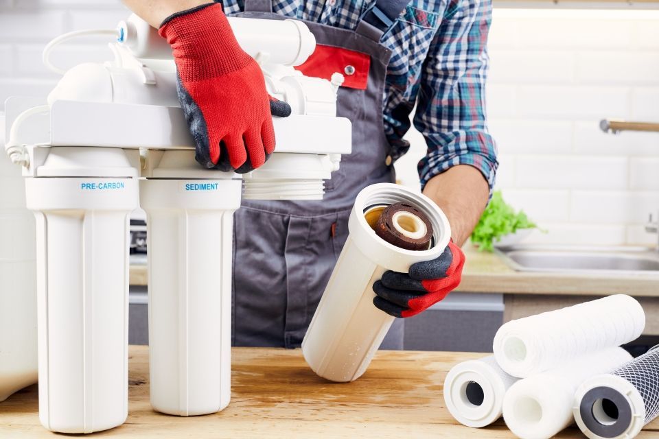 A person in red gloves changing a water filter in a kitchen setting.
