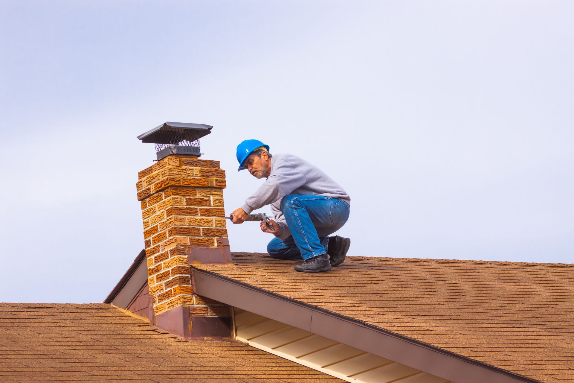 Contractor with blue hardhat on the roof repairing the chimney.