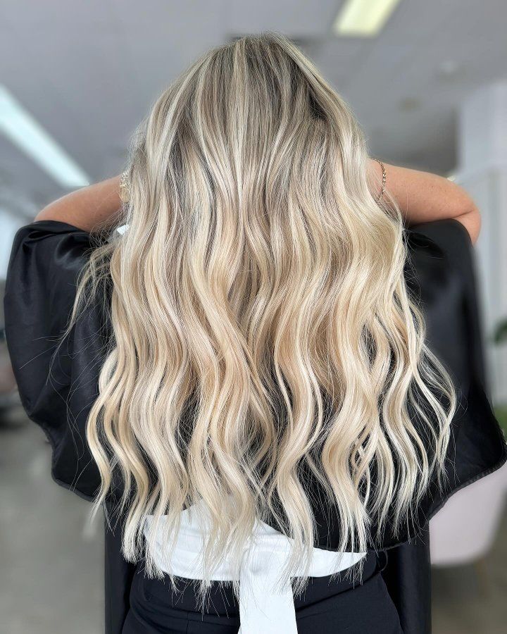 A Woman With Long Blonde Wavy Hair Is Standing In A Salon — The Hair Boutique Co In Varsity Lakes, QLD