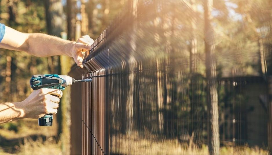 Fence installer holding a hand drill installing a metal fence panel.
