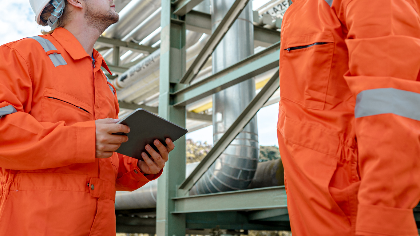 Workers in hard hats reviewing a checklist at an industrial refinery site