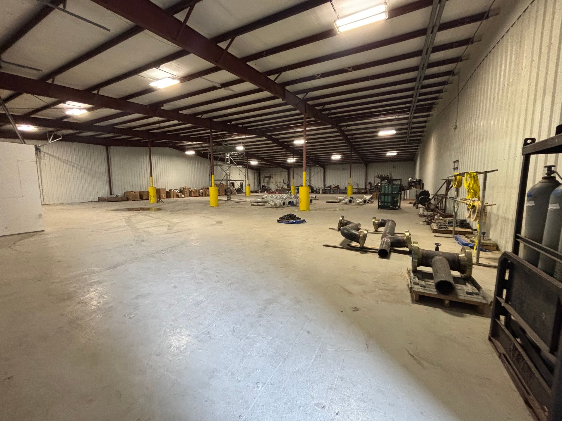 Spacious empty warehouse with metal beams, concrete floor, and equipment scattered near the walls