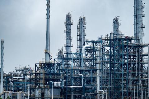 Worker in hard hat overlooking a scaffolded industrial structure under a cloudy sky.