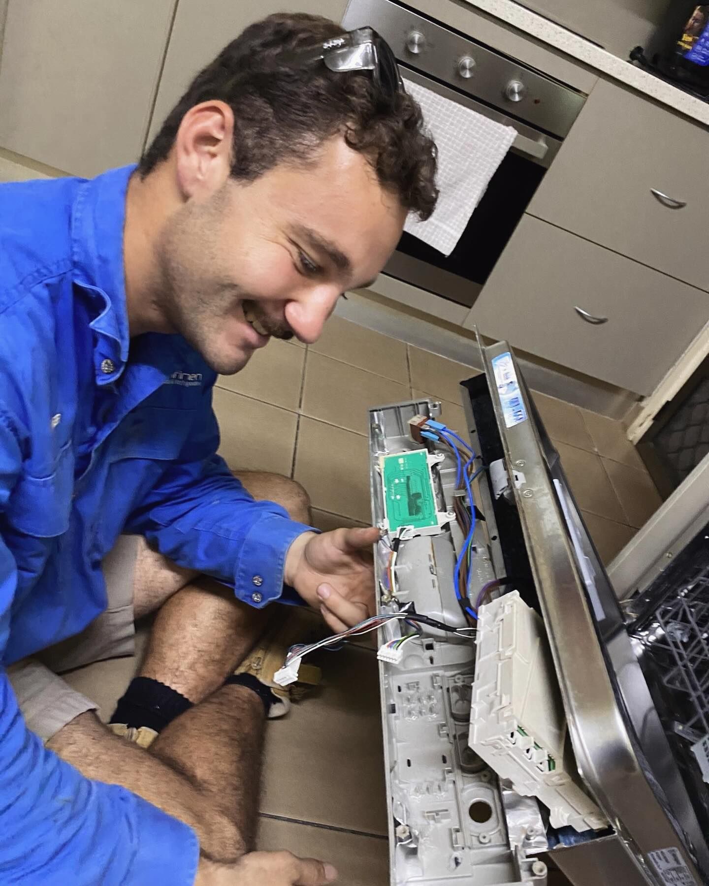 Man in Blue Shirt Repairing Dishwasher. Kitchen Setting — Lahtinen Electrical & Refrigeration in Ingham, QLD