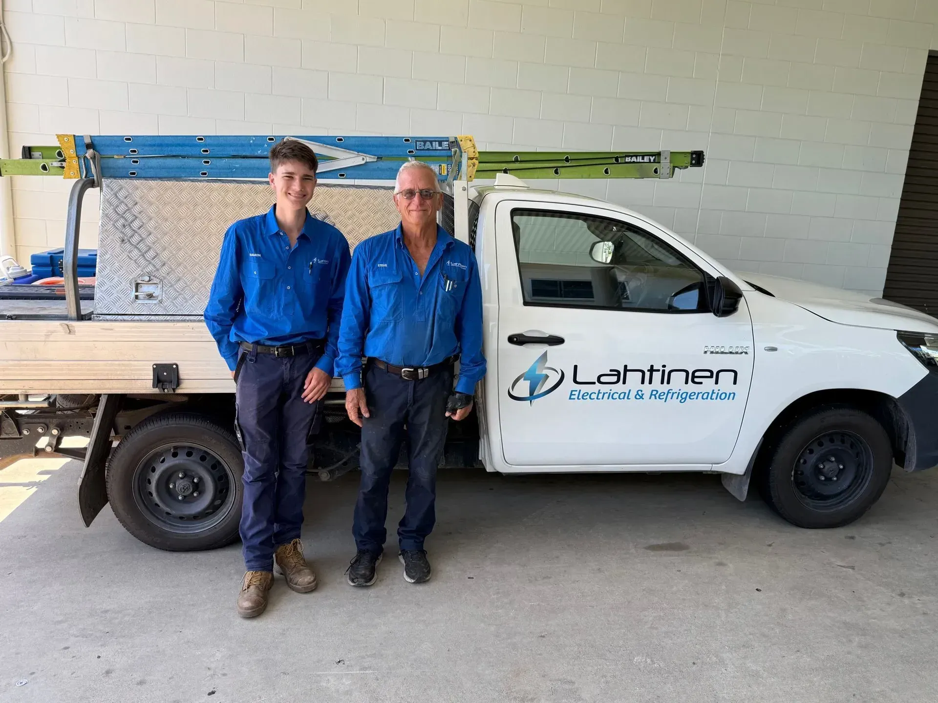 Two People in Blue Work Shirts Stand Next to a White Work Truck — Lahtinen Electrical & Refrigeration in Ingham, QLD