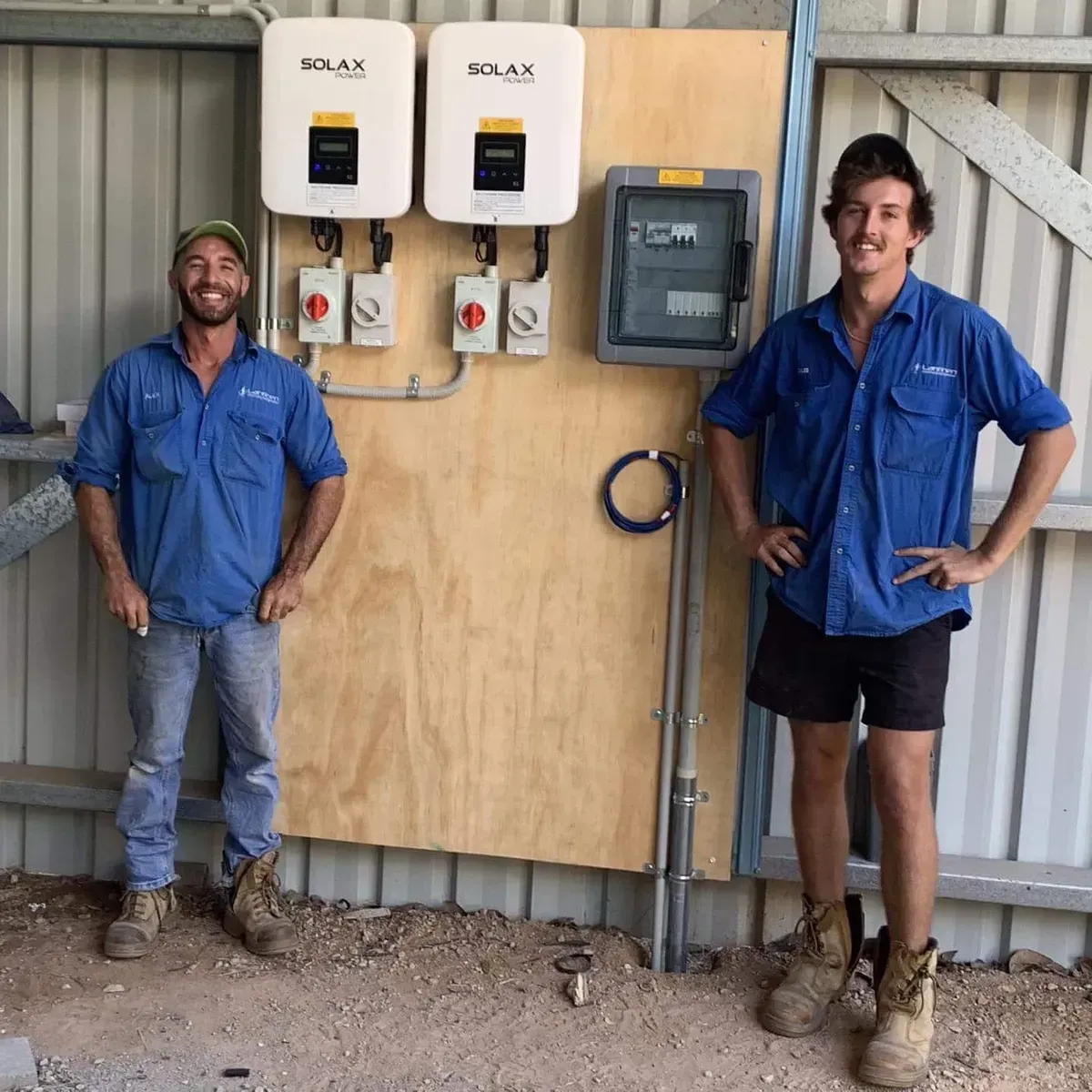 Two Men in Blue Shirts Stand Beside Solar Panel Equipment — Lahtinen Electrical & Refrigeration in Ingham, QLD