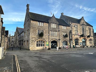 Stone buildings on a quiet street corner under a blue sky, with parked cars and pedestrians nearby