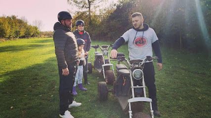 Three people stand with go-karts on a grassy path in a sunny park.