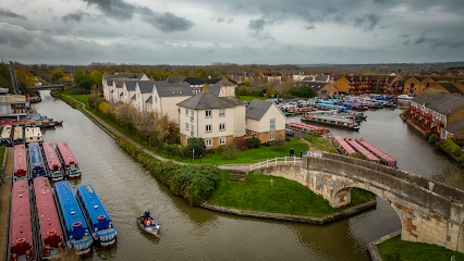 Canal with moored narrowboats beside a stone bridge and white houses under a cloudy sky