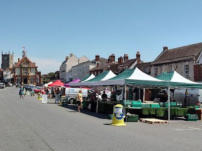 Outdoor market stalls with green-and-white canopies along a street beside a church on a sunny day
