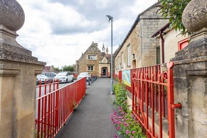 Narrow walkway beside red railings and stone buildings leading toward a house under a cloudy sky