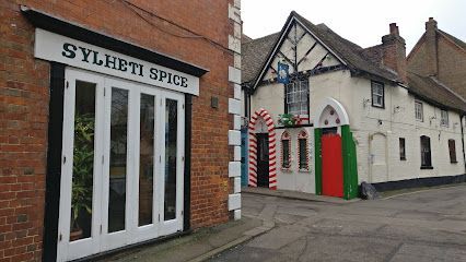 Street corner with Sylheti Spice shopfront and a white building with a green door and red-striped entrance.