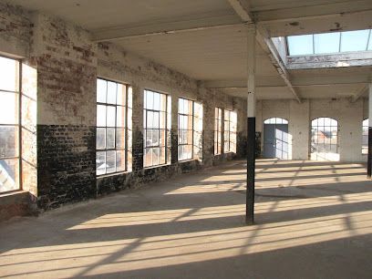Empty loft with large factory windows, brick walls, and long sunlit shadows on the floor