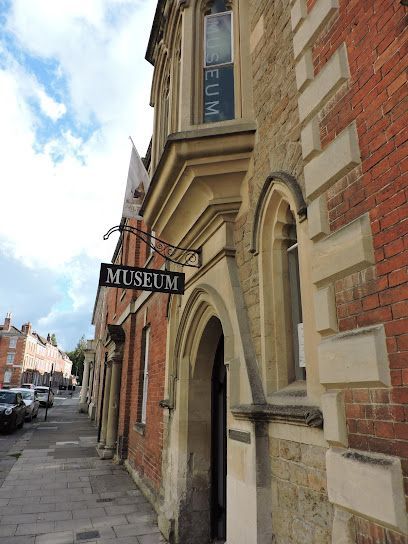 Street view of a historic museum entrance with a hanging “MUSEUM” sign on a brick building