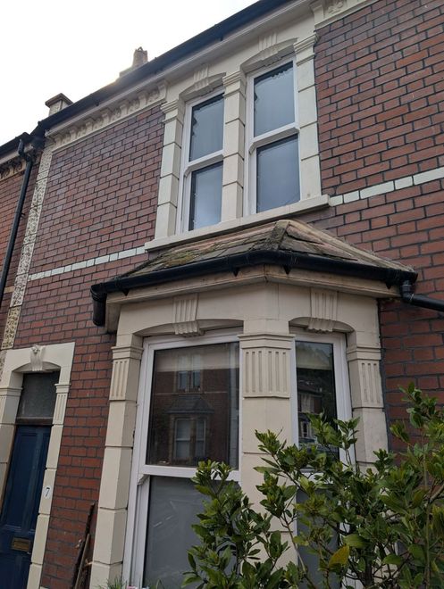 Red-brick house front with a white bay window and small porch roof, viewed from the street.
