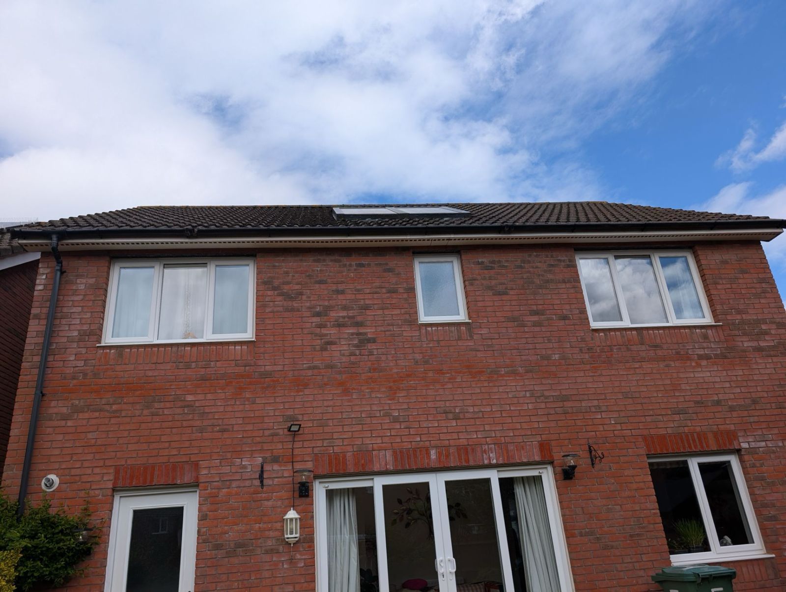 Red-brick two-story house with white-framed windows and a cloudy blue sky above