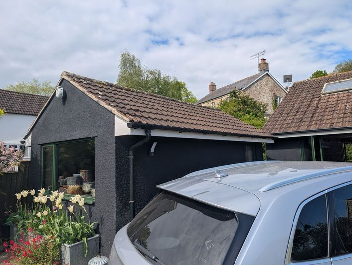 Suburban house with tiled roof and garden, partly obscured by a blue car in the foreground
