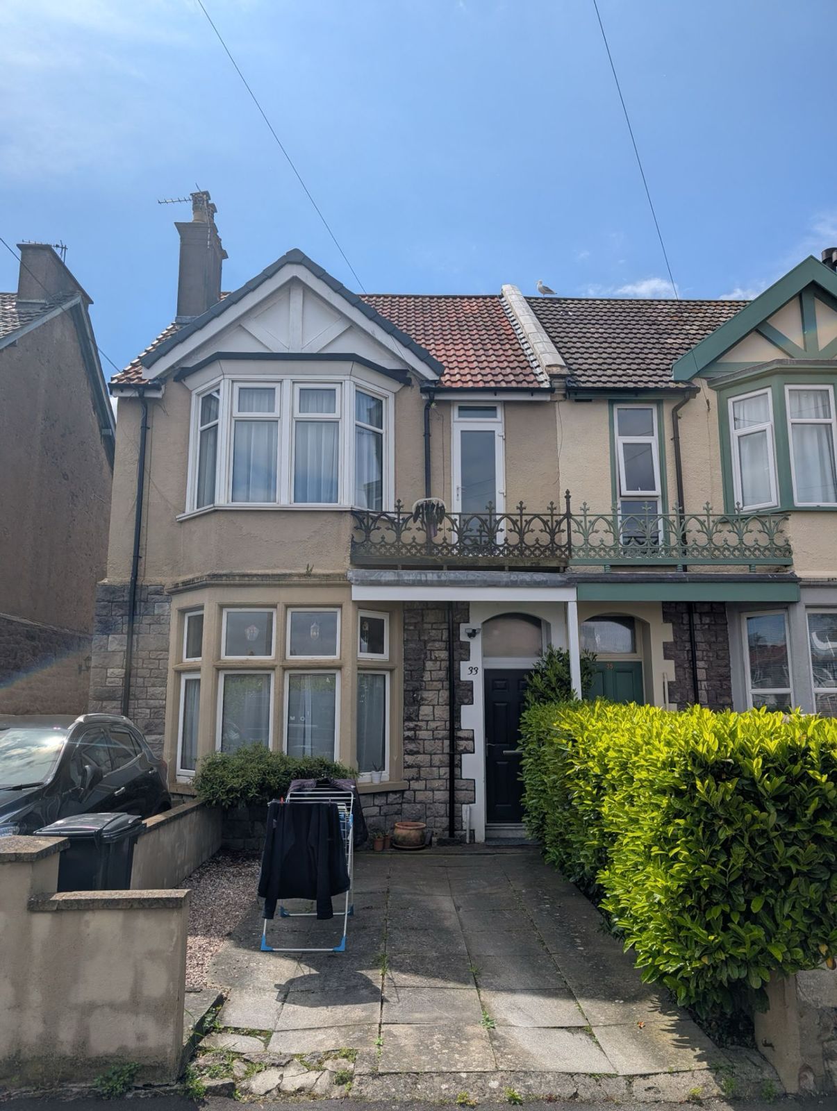 Semi-detached house with bay windows, tiled roof, front garden, and a hedge-lined path under a blue sky