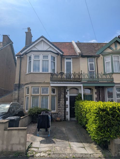 Semi-detached house with bay windows, tiled roof, front garden, and a hedge-lined path under a blue sky
