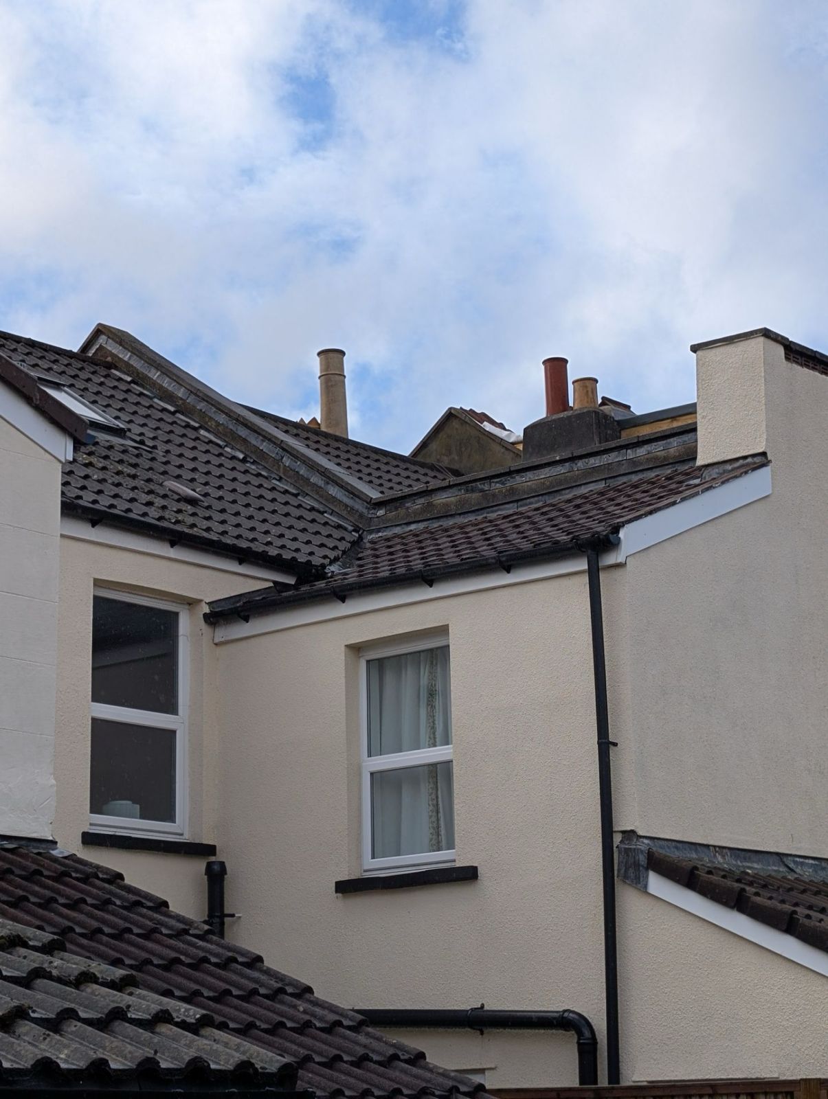 View of white and beige house rooftops and chimneys against a cloudy sky