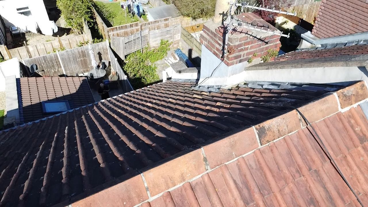 View from a rooftop with corrugated metal roofs and neighboring houses below in bright sunlight