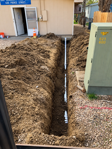 Trench dug beside a beige house, exposing a white pipe near a utility box in the yard.