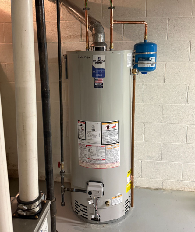 Water heater in a basement utility area with metal ductwork and pipes.