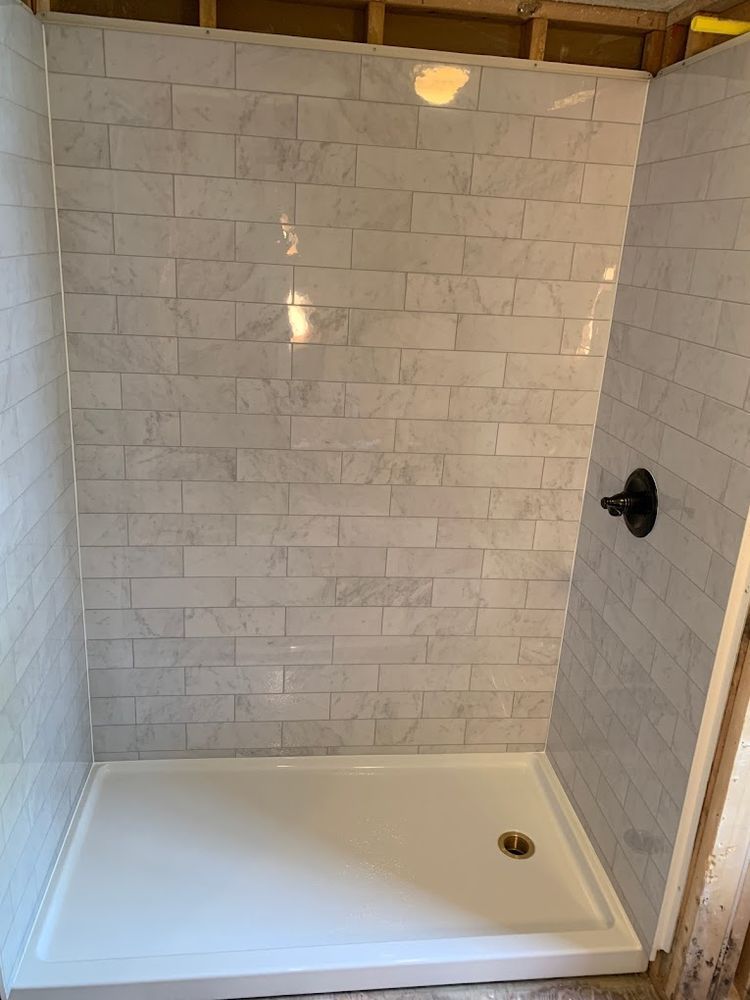 Tiled shower stall with white tub, white subway tile walls, and black shower control.