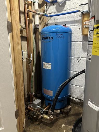 Blue water softener tank in a utility closet beside pipes and a water heater