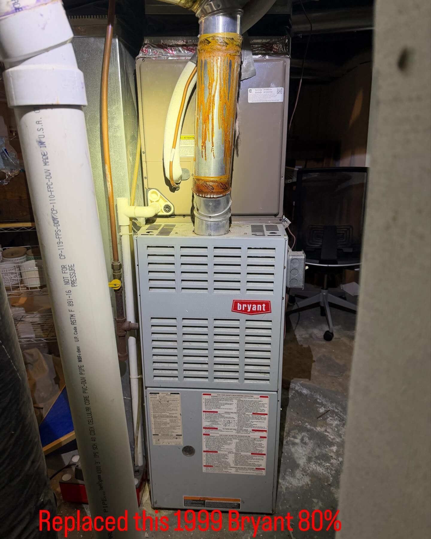 A Bryant furnace in a utility room. Gray, with rust on the vent. White PVC pipe to the left.